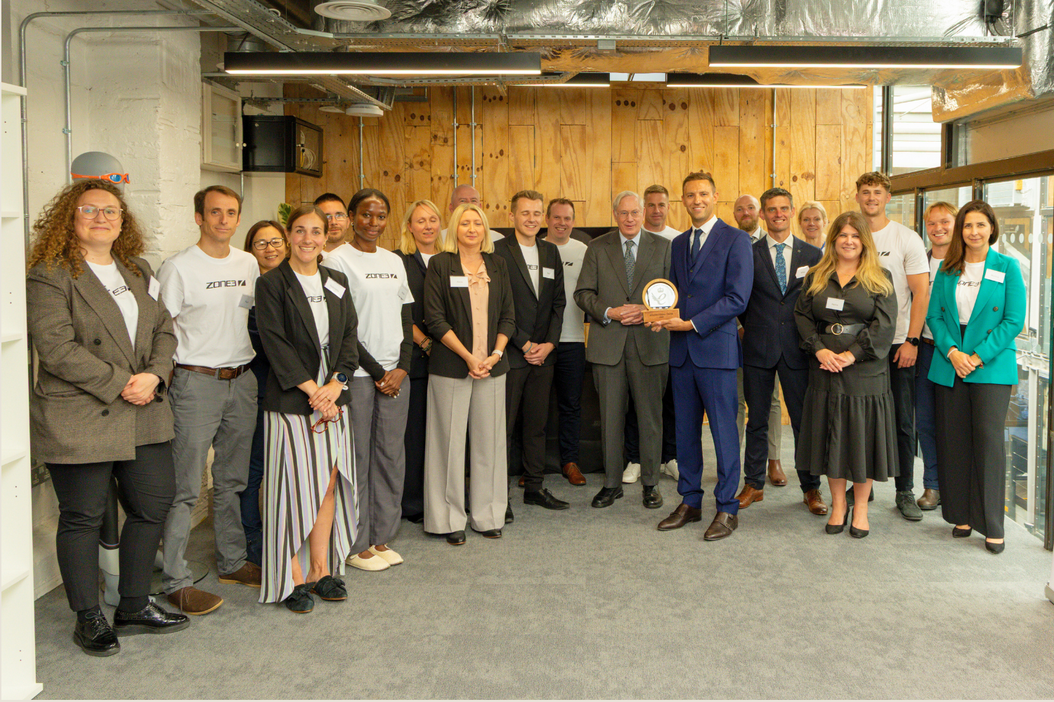 ZONE3 employees posing for a photo in an office setting with a James Lock holding an award. The Duke of Gloucestershire is standing next to James Lock