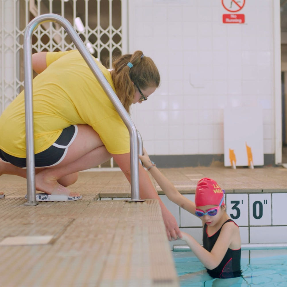 Image of a level water staff member assisting a child in a swimming pool.