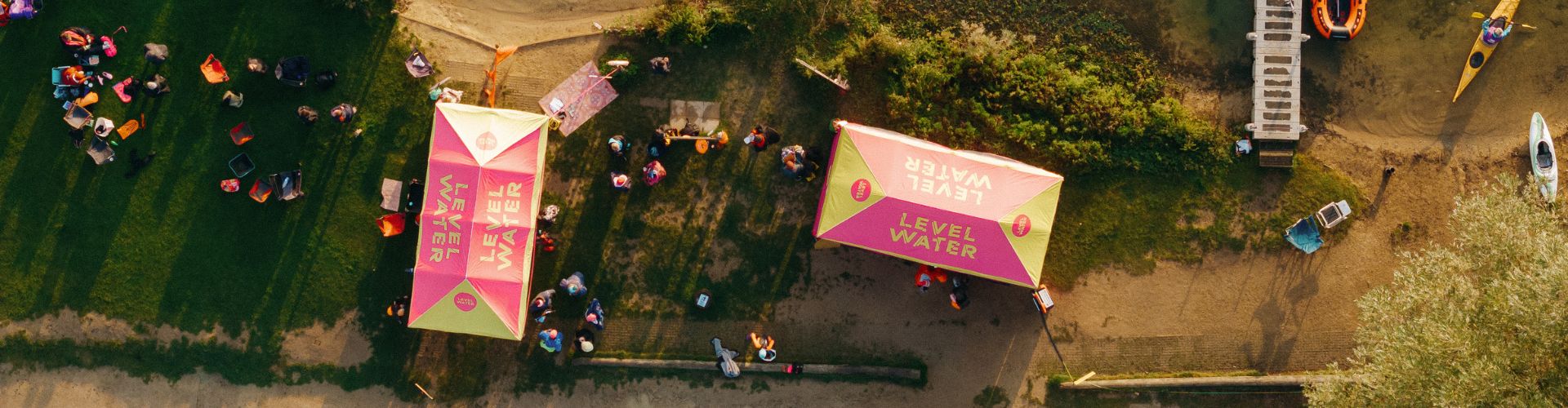 Top down view of the Level Water tents by a body of water. There are groups of people around the marquees. Boats are in the right corner.
