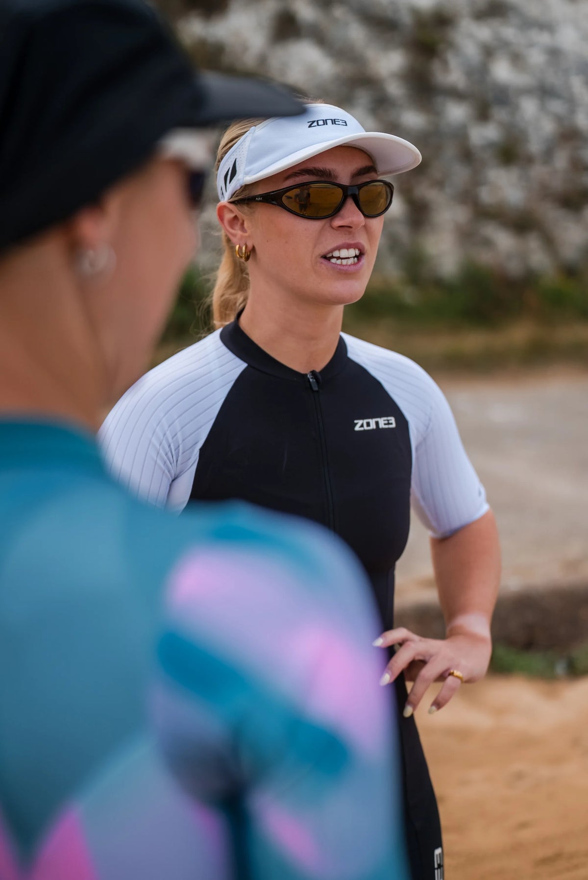 two women standing both wearing sunglasses and the black and white running visor with a zone3 logo on a blurred background.