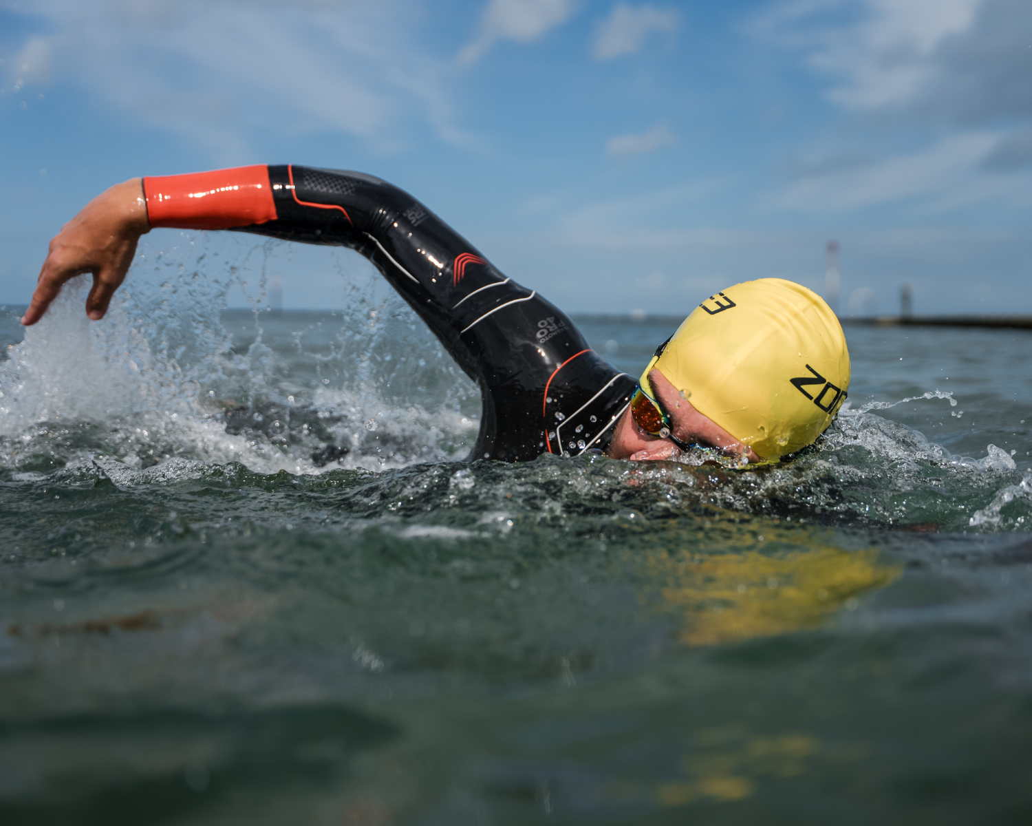 Person swimming in open water wearing a Vanquish-x Wetsuit and yellow swim cap.