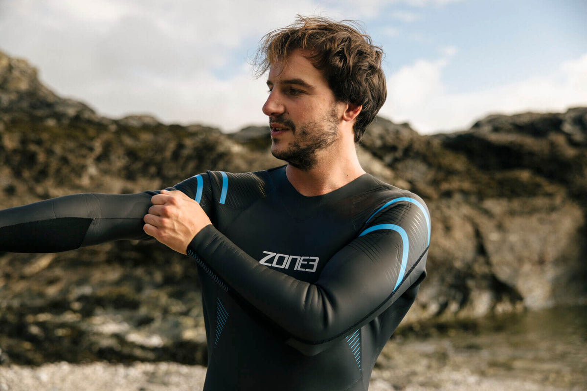 Man putting on Zone3 Glide wetsuit at the beach.