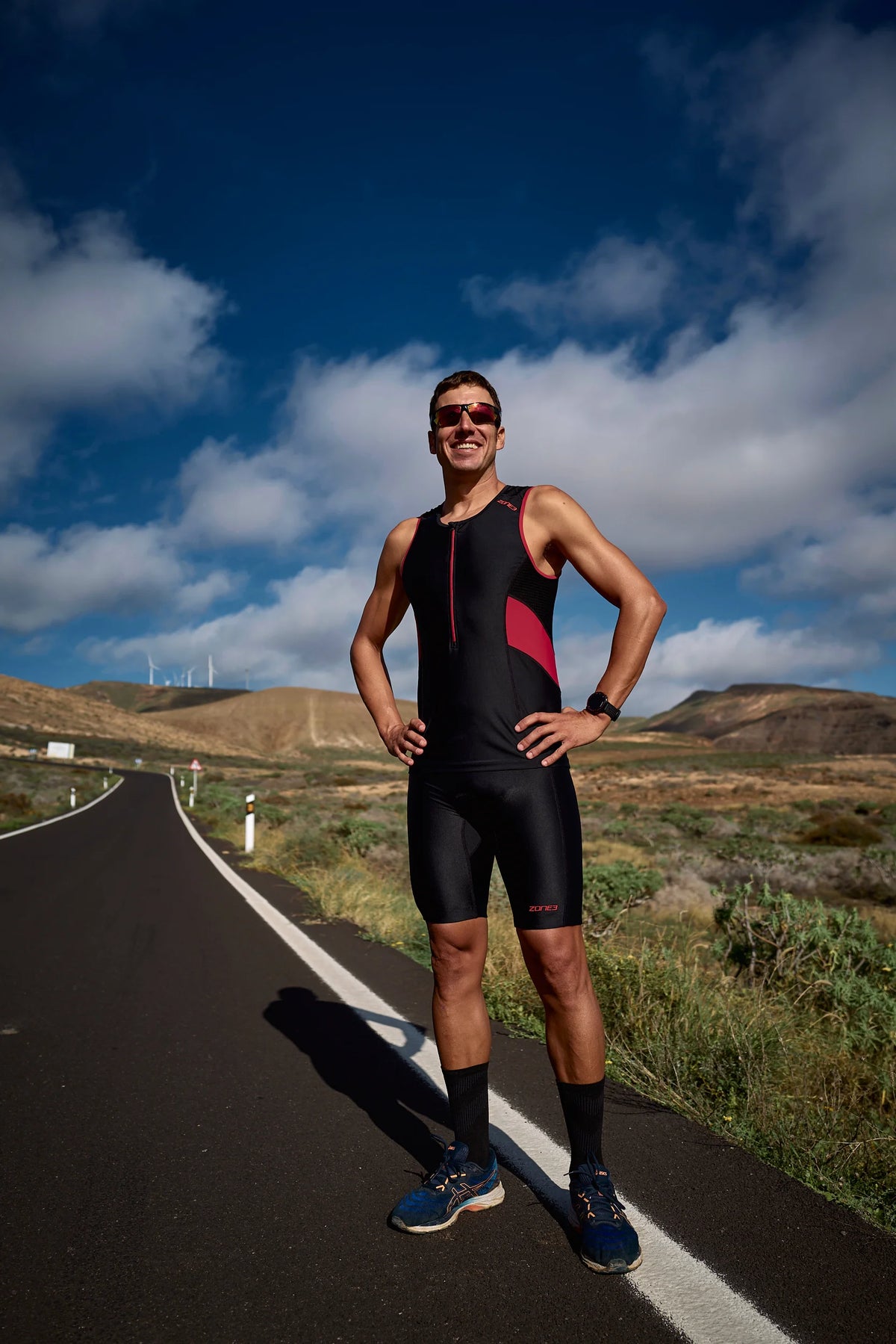 Man wearing the Zone3 triwear Activate in a black and red standing on the side of a road.