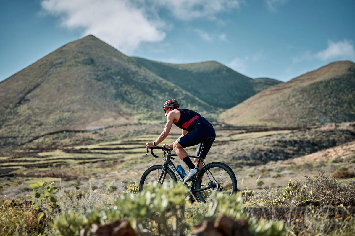 A cyclist wearing the Zone3 triwear Activate riding a bike through the mountain landscape under a blue sky.