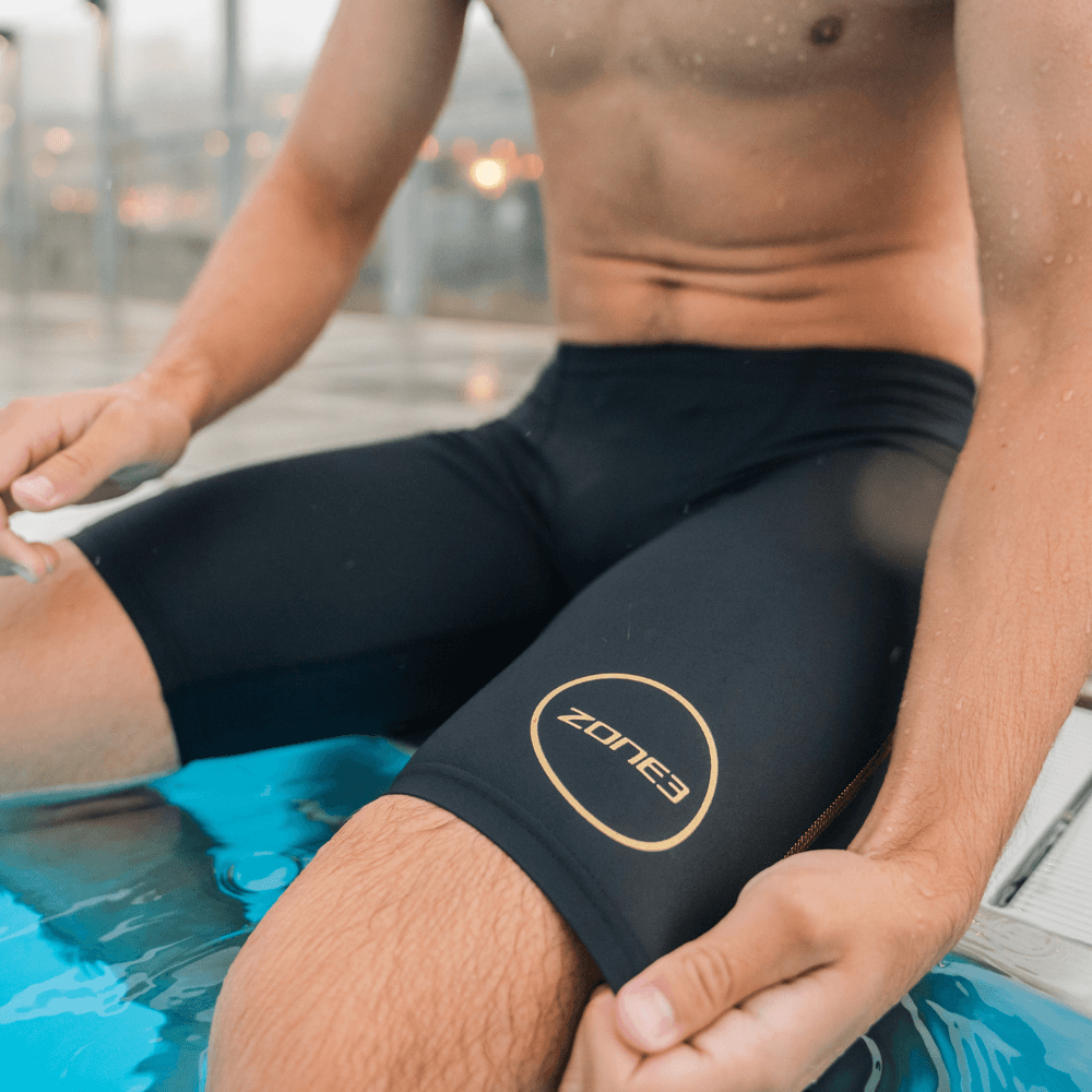 Close-up of a swimmer wearing a black MF-X jammer with a gold circular logo