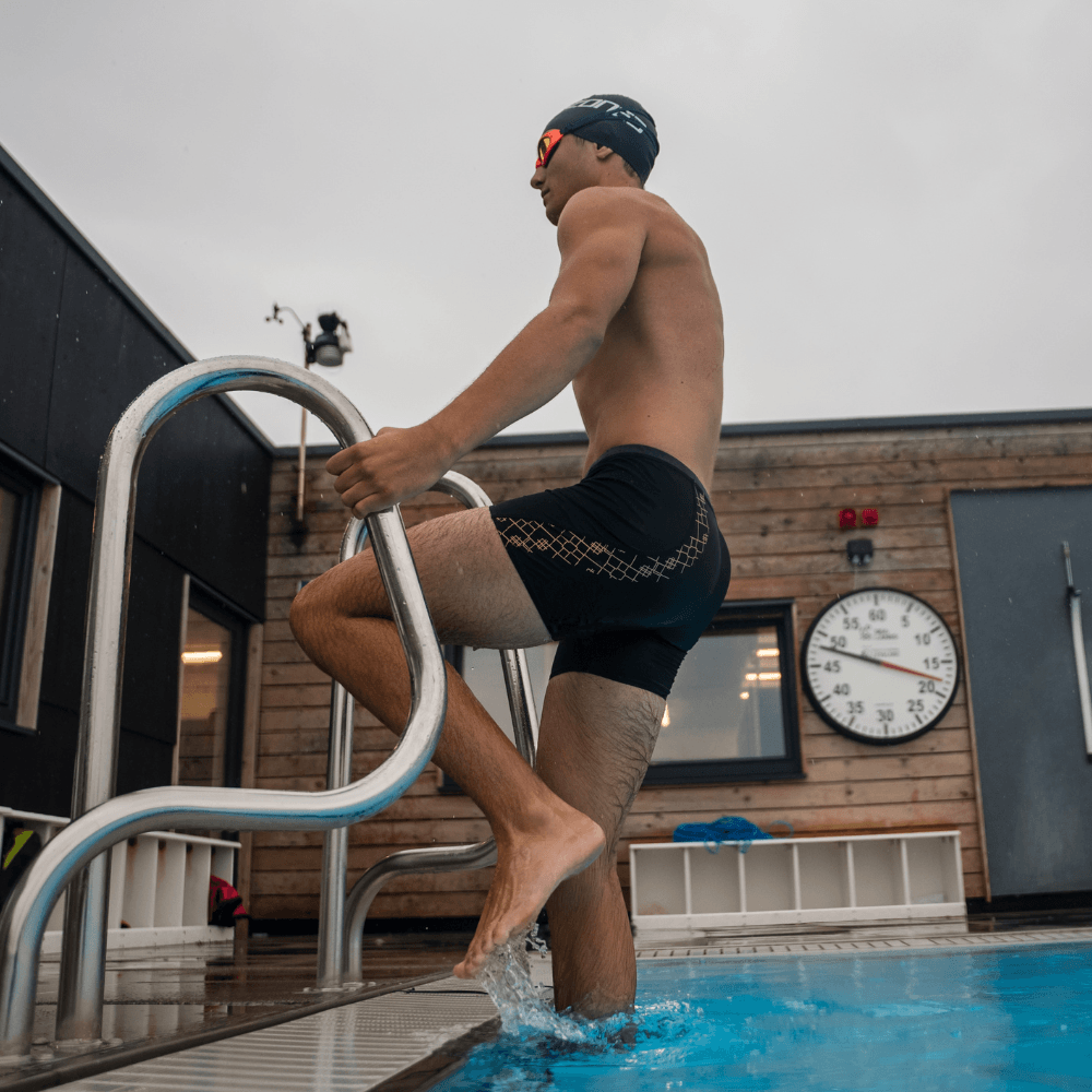 Swimmer in a black MF-X jammer with a gold geometric pattern stepping from the pool edge