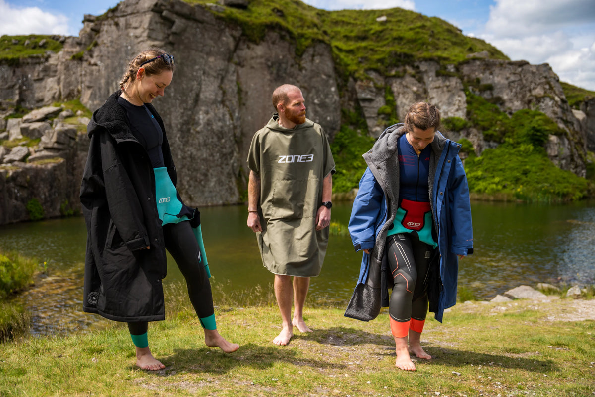 Three people standing by a body of water. Man in the middle wearing the Khaki Microfibre Changing Robe. with rocky cliffs in the background.