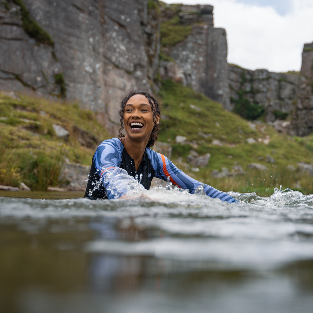 Person wearing long sleeve swimsuit smiling while partially submerged in natural water pool