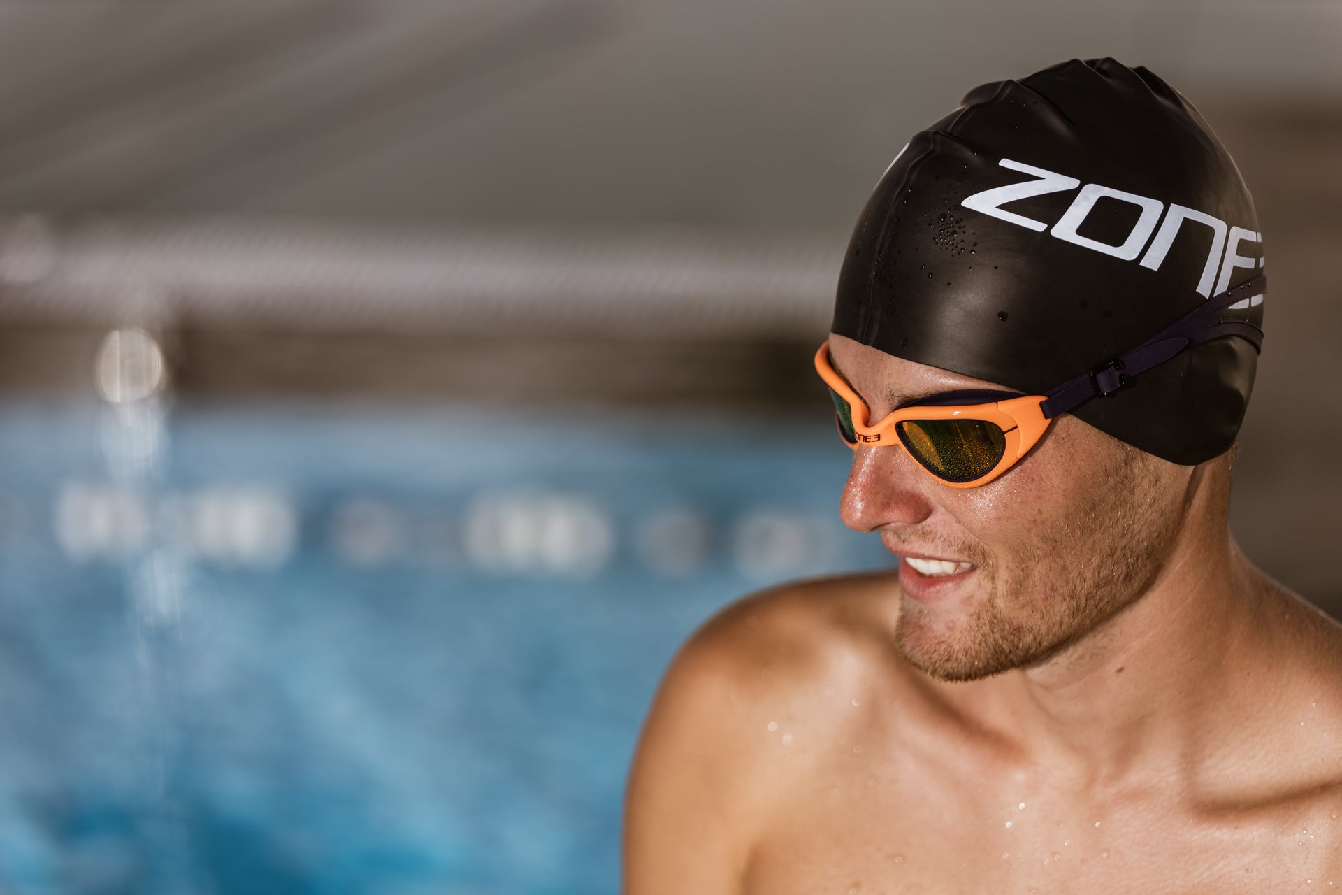 Man wearing a Zone3 swim cap and goggles by a pool