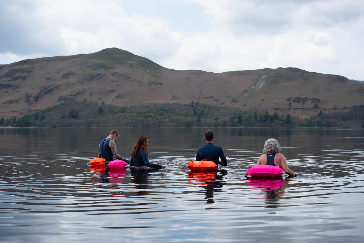 Four people in the water. in Zone3 gear  and the Recycled Safety Buoy Dry Bag 28L in pink and orange. 