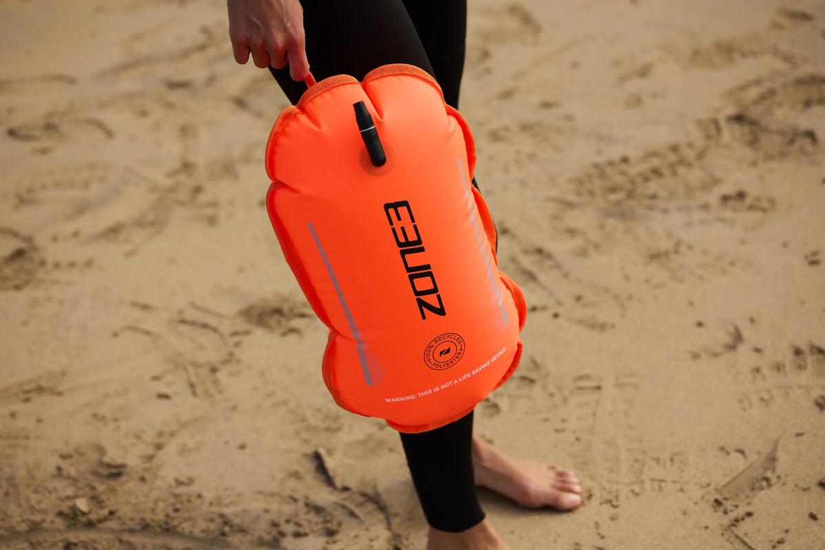 athlete holding the Recycled Swim 
Safety Buoy Tow Float at the beach. 