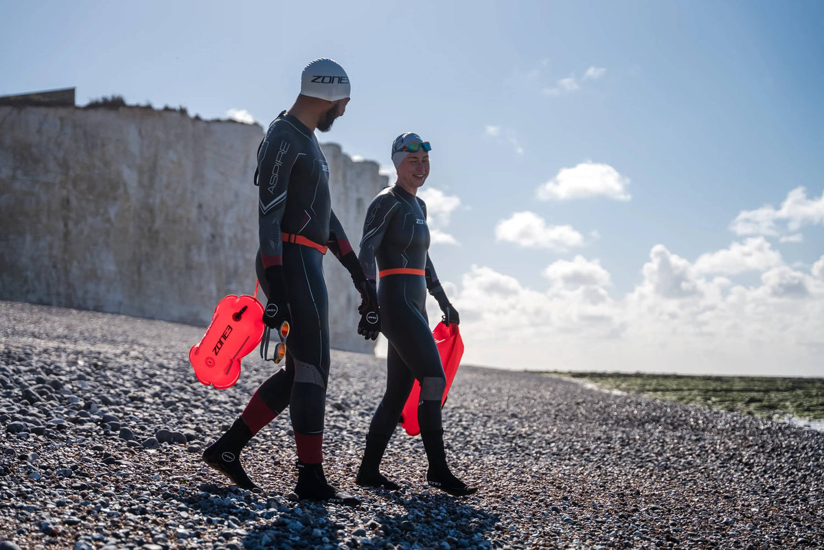 two athletes walking into open water holding the Recycled Swim 
Safety Buoy Tow Float at the beach. 