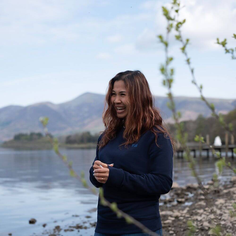 A Women standing by a lake wearing the Zone3 Seathwaite Crew Neck Sweatshirt in Navy paired with jeans. 