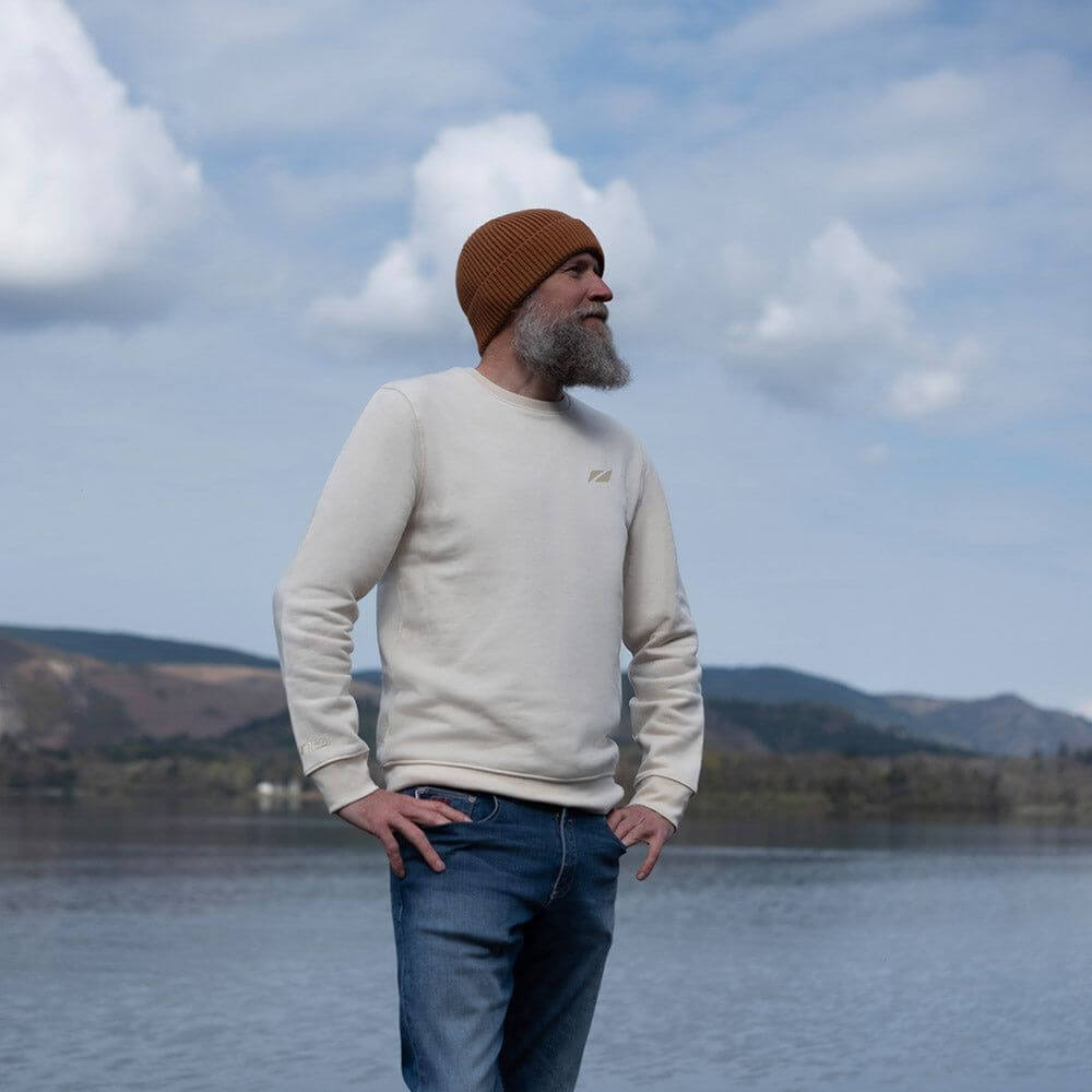 A Man standing by a lake wearing the Zone3 Seathwaite Crew Neck Sweatshirt in white paired with jeans. 