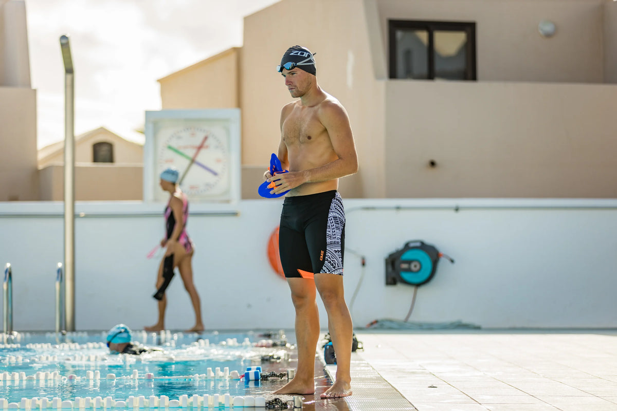Athlete standing by the pool holding the Zone3 Power Stroke Swim Paddles.