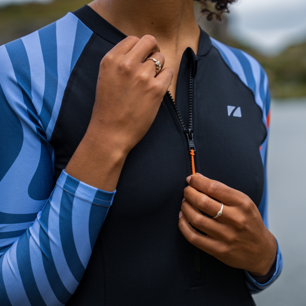 A woman wearing a ZONE3 OWS swimsuit. She is adjusting the front zipper and neck