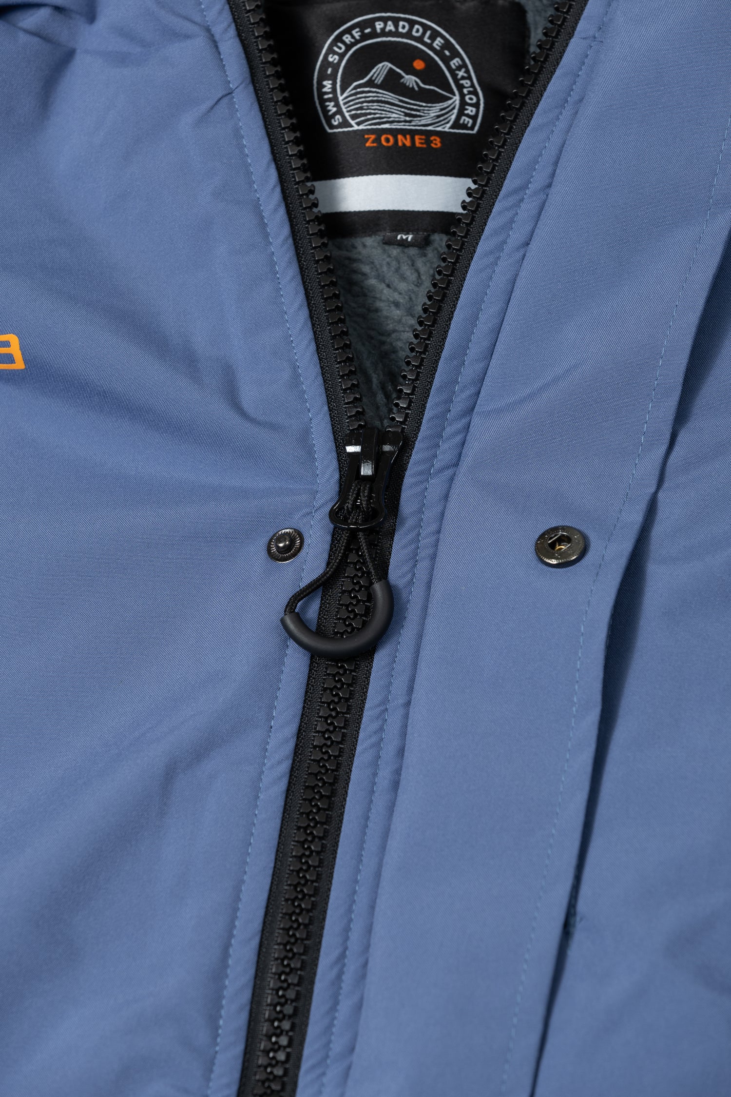 Close-up of the robe’s front zip, with visible branded pull tab and logo patch inside the collar.