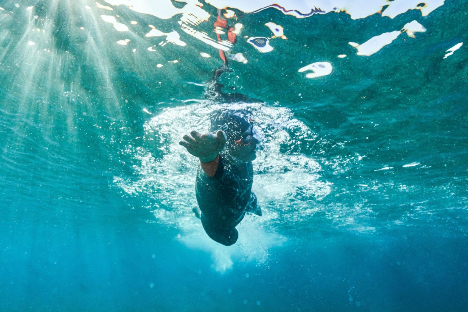 Person swimming underwater in a ZONE3 Vanquish-X wetsuit. They are in clear blue water with sunlight filtering through.