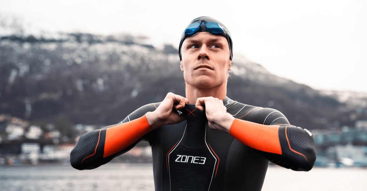 Casper Stornes close up wearing the Vanquish-X Wetsuit in black with Orange detailing. blurred background. 