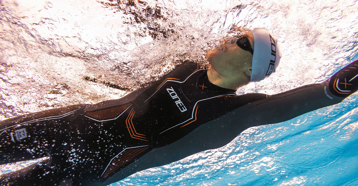 Casper swimming in a pool wearing he Zone3 wetsuit Vanquish-X and white Zone3 swim cap.