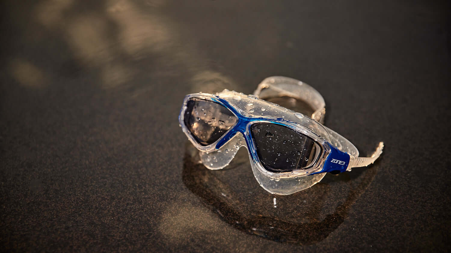 Vision Max Clear goggles with blue straps on a dark surface