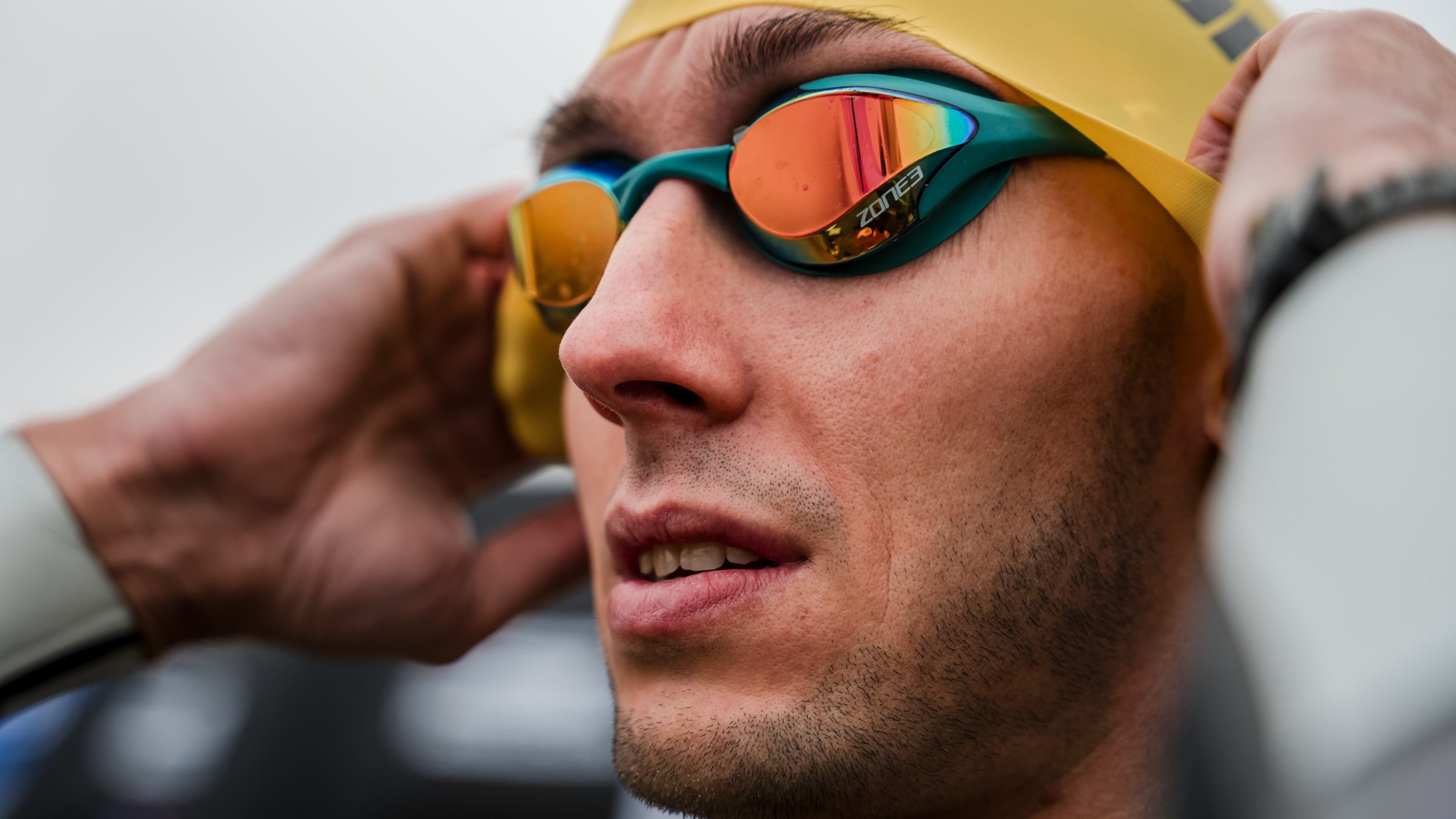 Male Athlete wearing a Zone3 swim cap and Volare Racing goggles with a blurred natural background. 