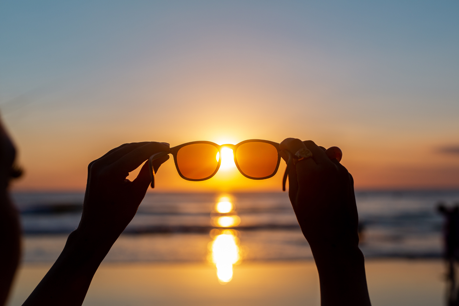 Sunglasses held up to the sunset over water