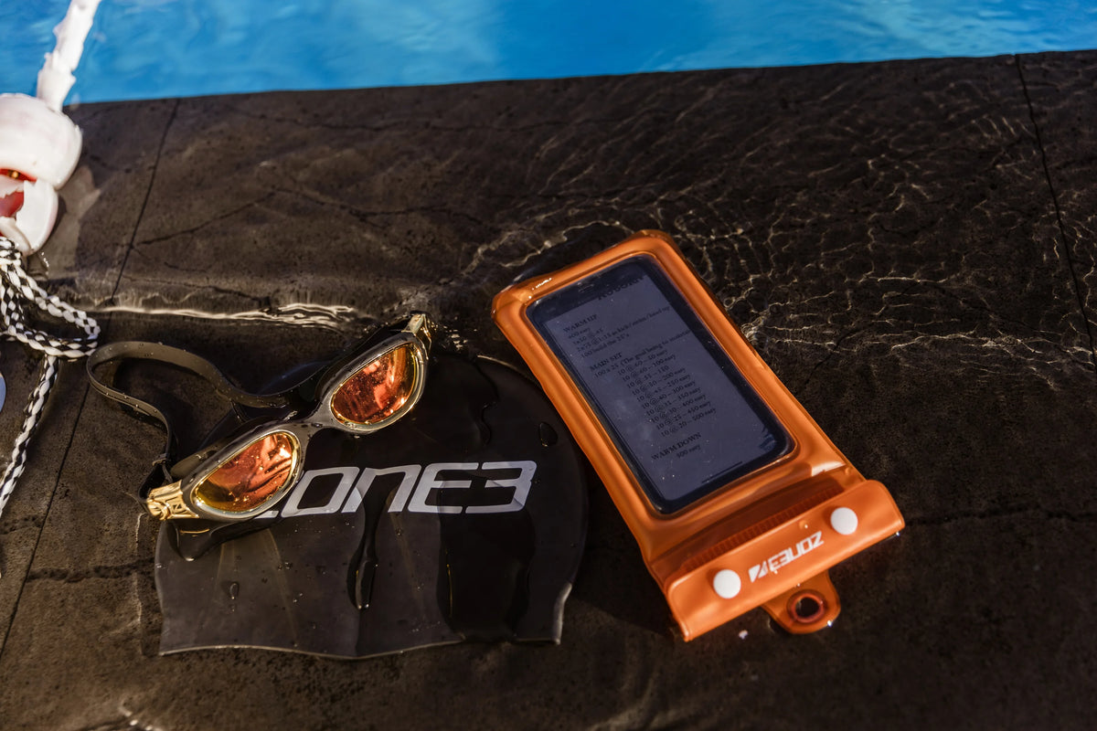 Zone3 water proof pouch, goggles and swim cap on the edge of the pool. 