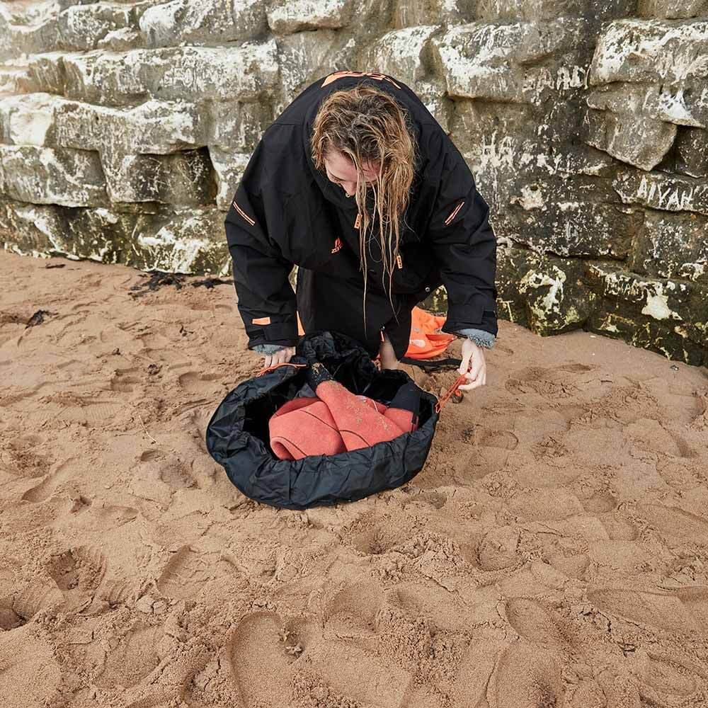 Women Athlete using the string feature on the Zone3 wetsuit changing mat to scope her wetsuit after changing. 