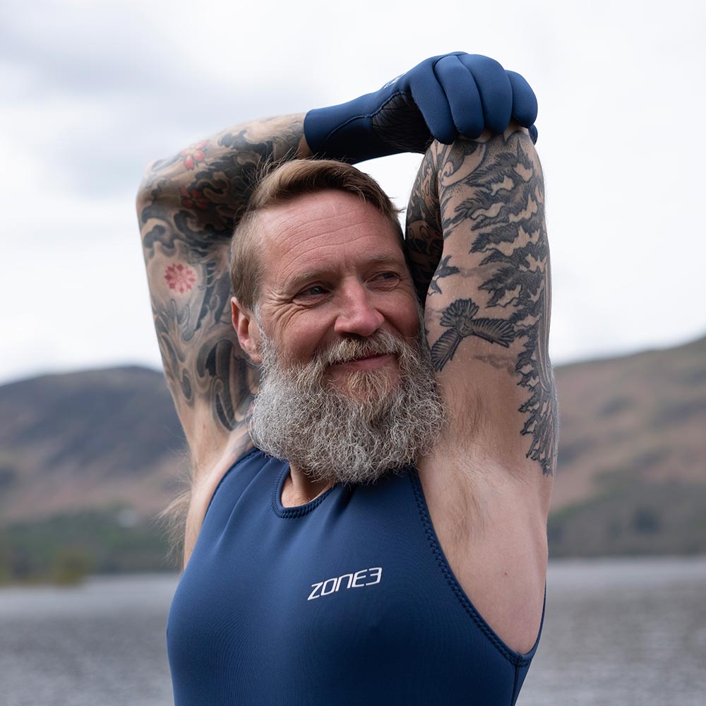 Man with tattoos wearing a Zone3 YULEX kneeskin and accessories by a lake