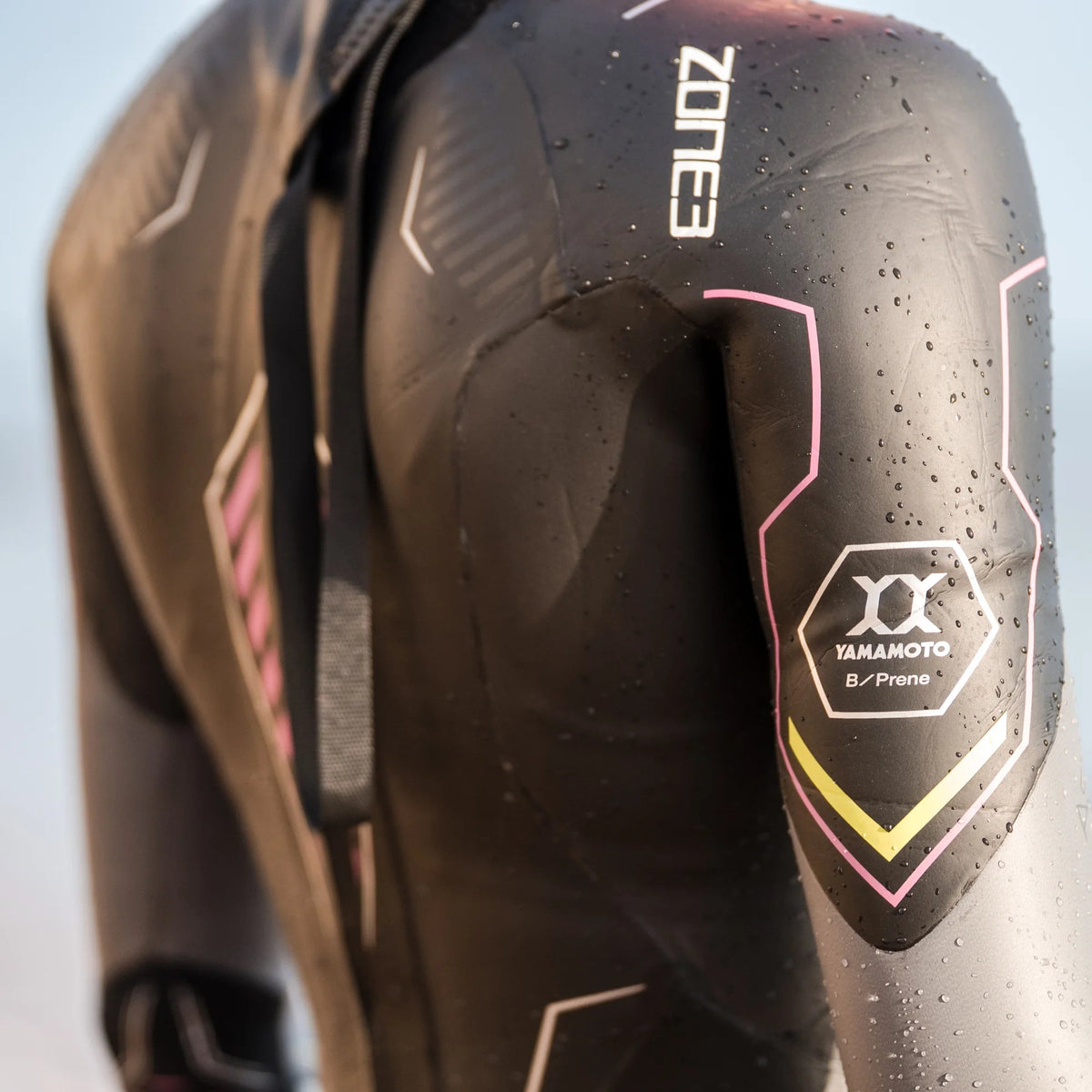 The back of someone wearing a black Zone3 wetsuit with gold and pink detailing.