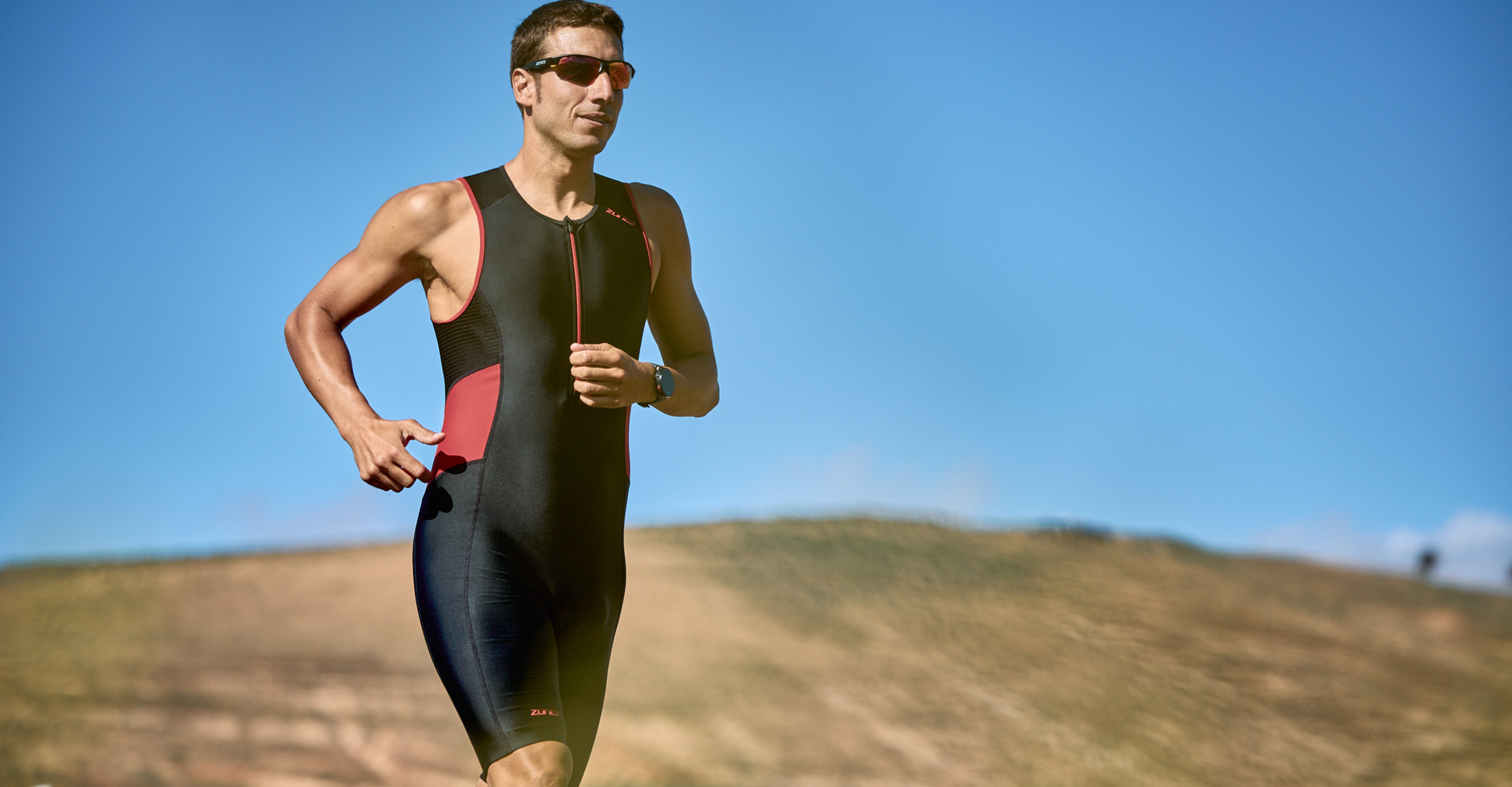 Man running outdoors in the red and black zone3 activate sleeveless trisuit on a clear day