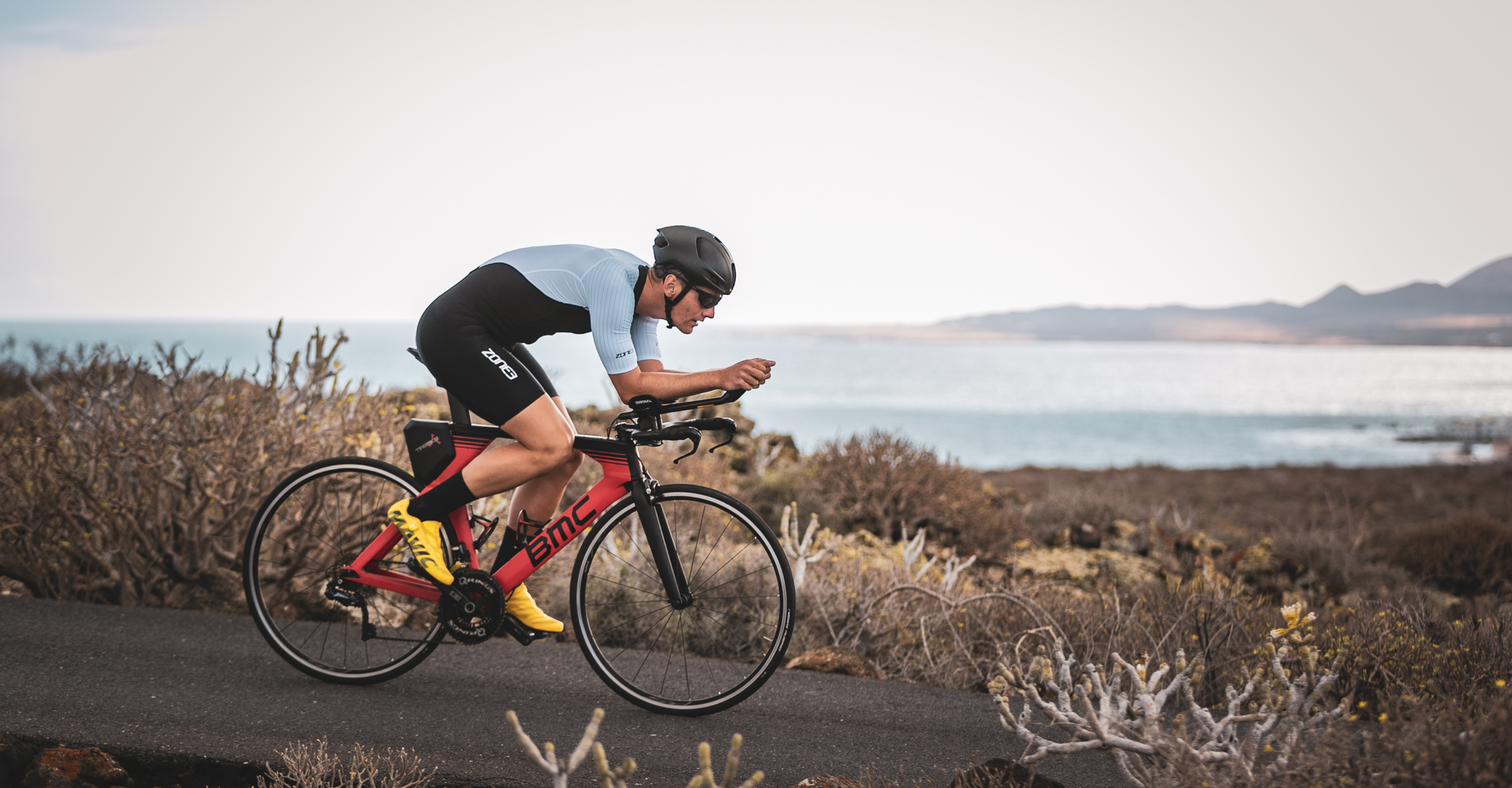 Person riding a bicycle in the lava trisuit on a trail with a scenic background