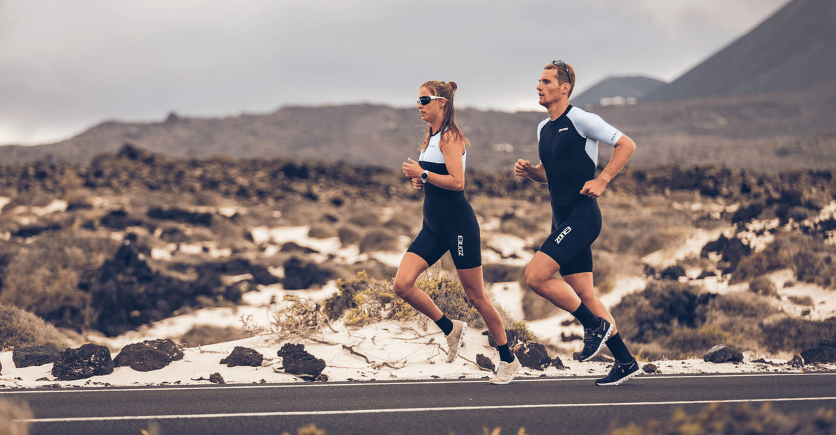 Two runners in lava trisuit running along a coastal road with ocean waves in the background.