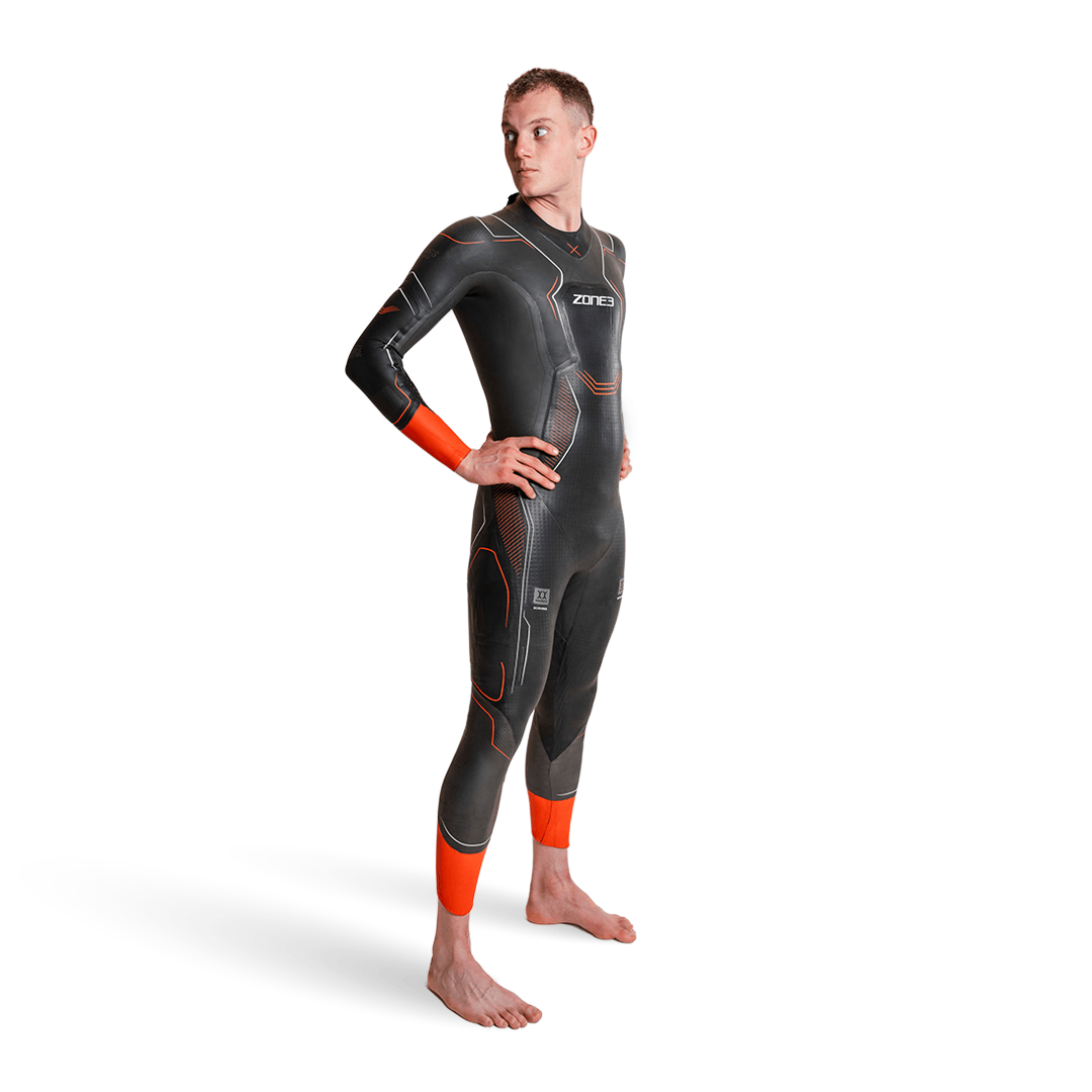 Mann trägt Vanquish-X-Neoprenanzug in Dunkelgrau mit orangefarbenen Manschetten und geometrischen Einsätzen.