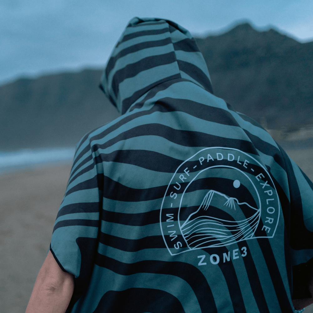 Athlete wearing the Zone3 Changing robe from the back displaying the logo at the beach. 