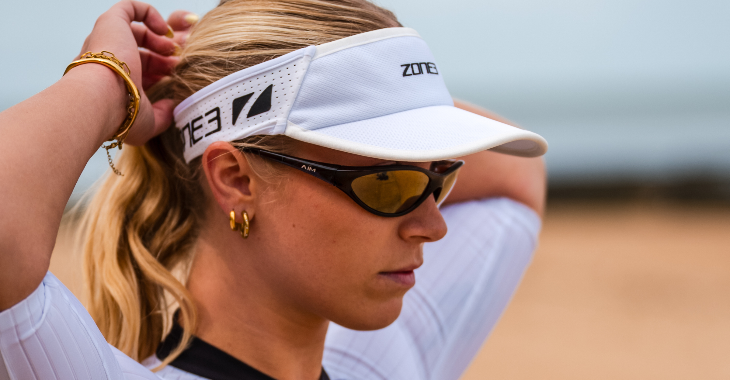 Woman wearing glasses and a zone3 white running visor with a zone3 logo on a blurred background