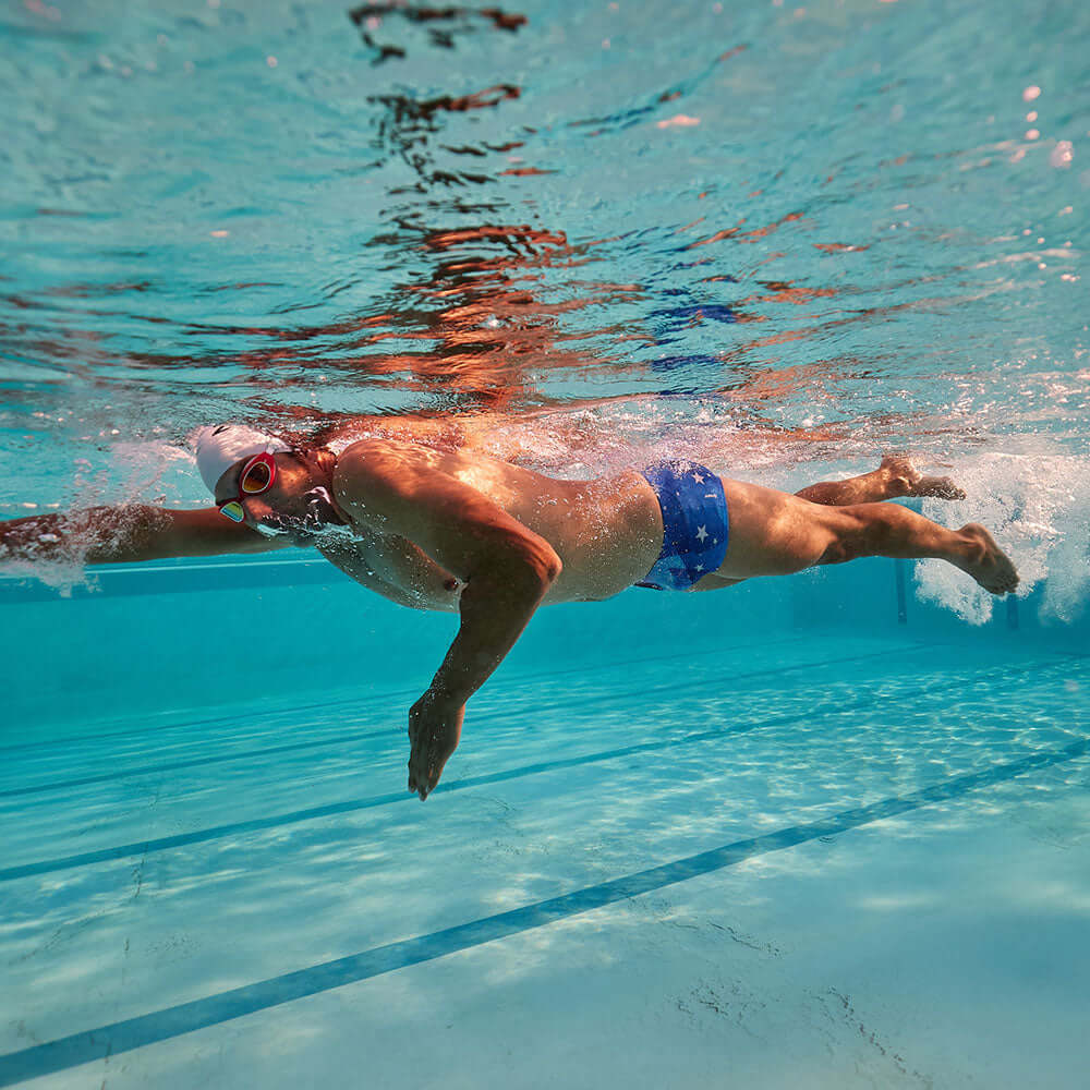 Athlete swimming in clear water wearing Brief Shorts (USA) featuring an American Flag design.