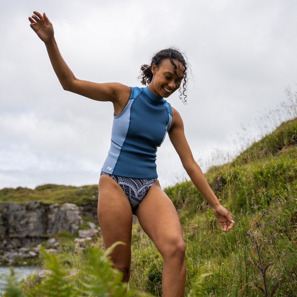 Woman joyfully wearing a Yulex® Vest while exploring nature, showcasing versatility for water activities.