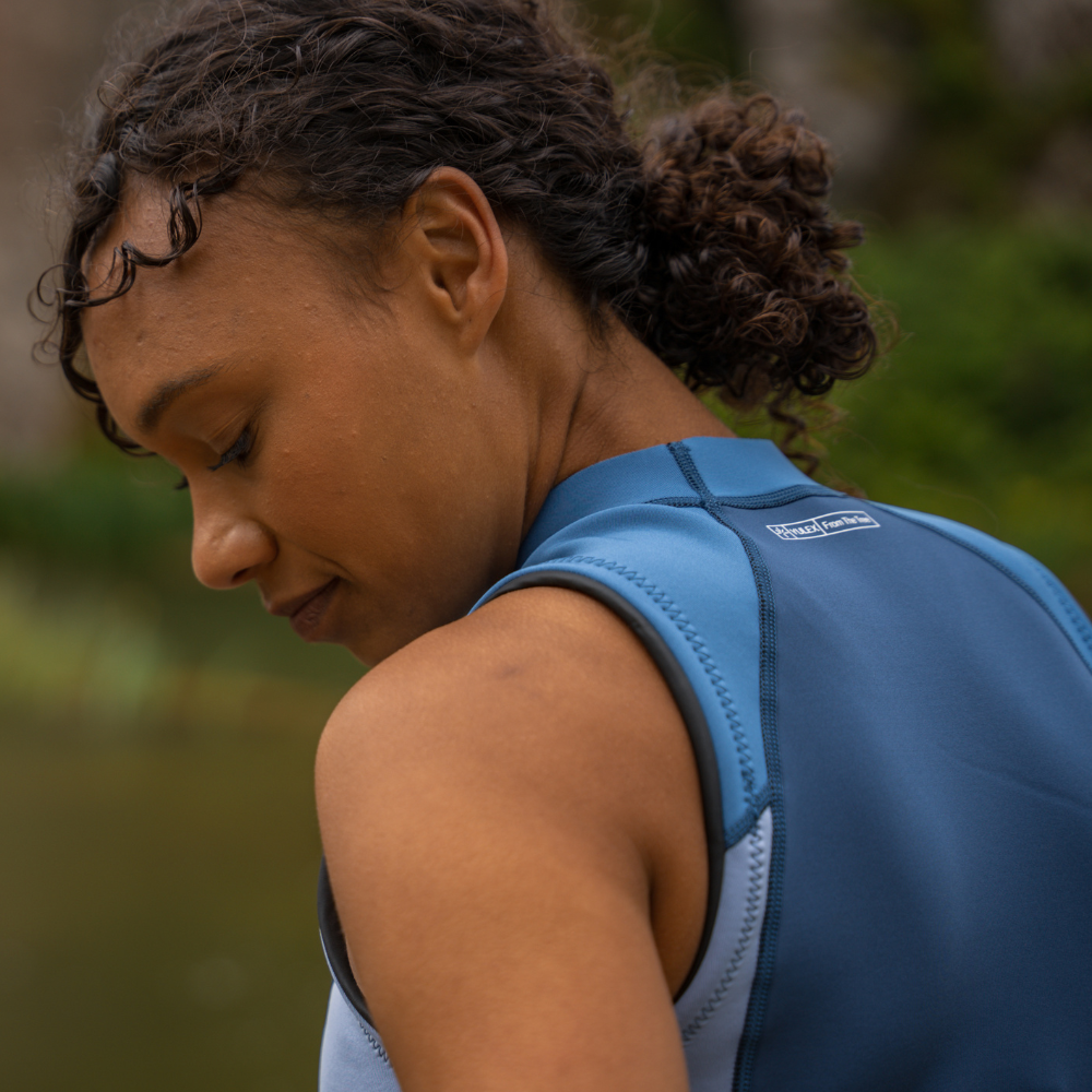 Woman wearing Yulex® Vest by the water, showcasing its sustainable material and design for water sports.