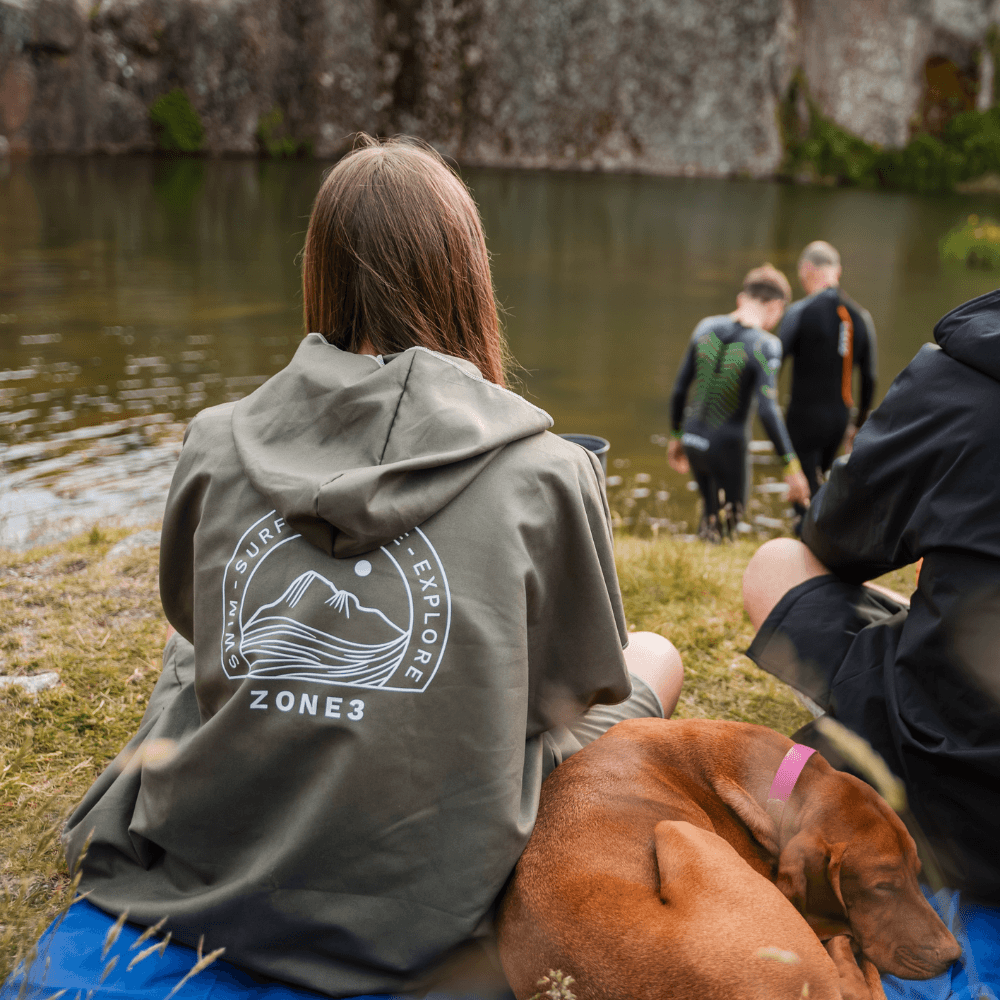Athlete wearing a Zone3 Microfibre Changing Robe in green sitting by a lake with a dog